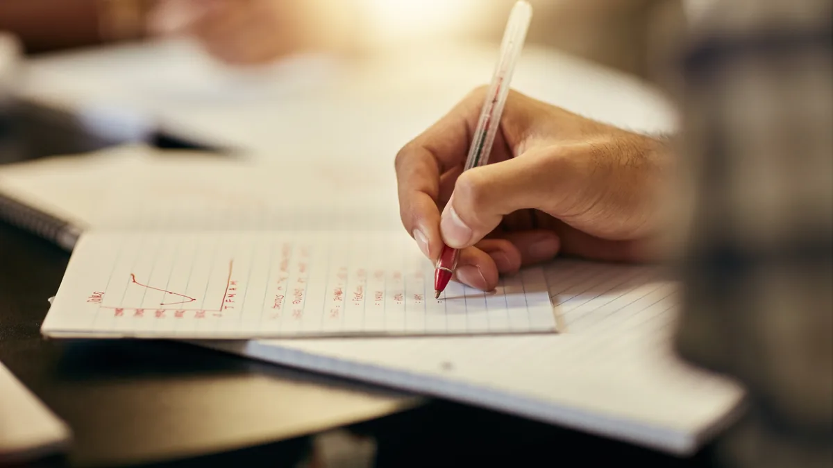 Mano tomando notas con bolígrafo en un cuaderno para elaborar un resumen.