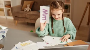 Niña sonriendo mientras memoriza letras con tarjetas de estudio (flashcards) sobre la mesa.