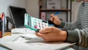 Persona usando una calculadora para revisar recibos y gastos sobre el escritorio.
