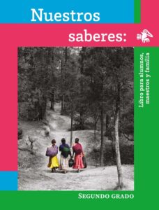 Portada de Nuestros saberes de segundo grado: fotografía en blanco y negro de un sendero entre árboles por el que caminan tres mujeres con ropa de colores