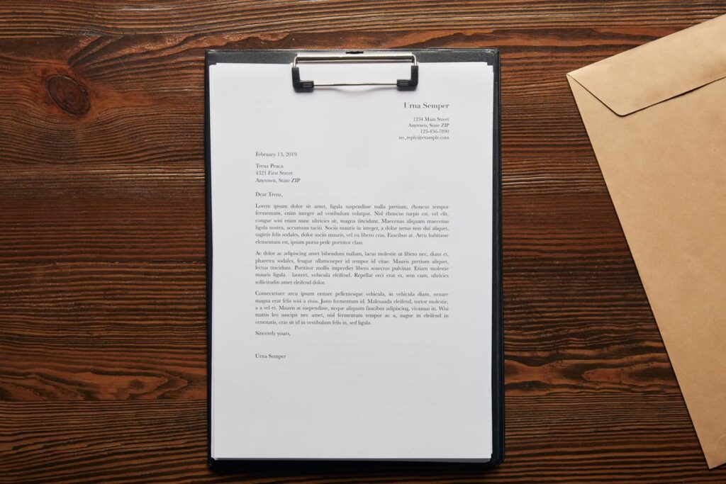 Carta formal impresa sobre un portapapeles junto a un sobre en una mesa de madera.