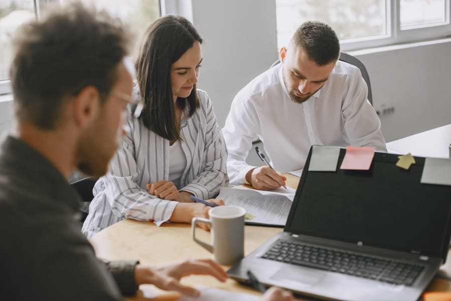 Equipo de trabajo revisando documentos junto a un ordenador portátil en una oficina